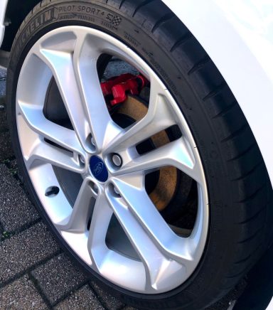 Close-up of a silver alloy wheel with a red brake caliper on a black tyre.